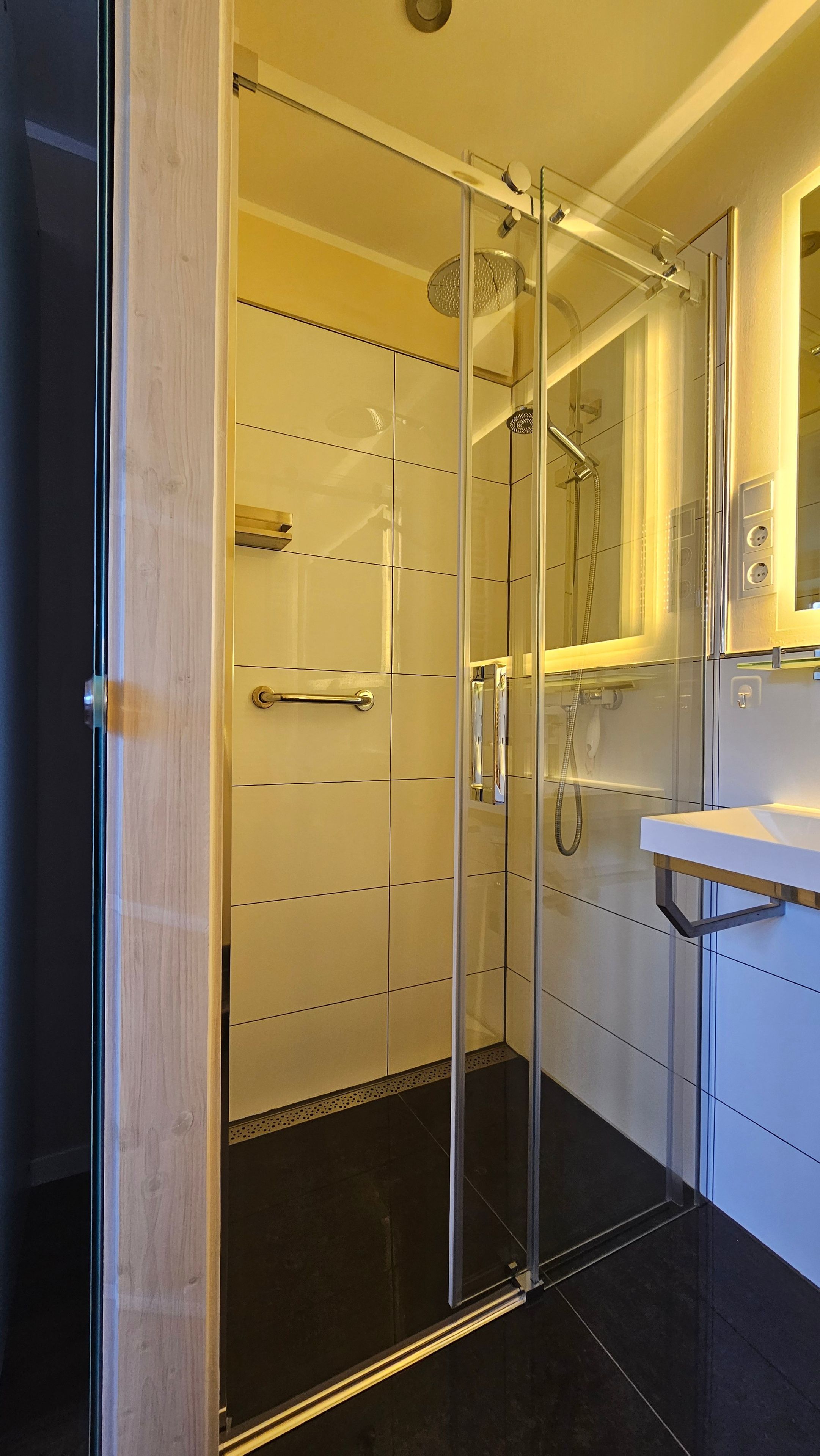 Een moderne badkamer met een douchecabine van glas, een witte wastafel en een spiegel erboven.