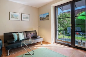 Una sala de estar con un sofá, una mesa de centro de vidrio y vistas a un espacio exterior con sillas y una mesa.