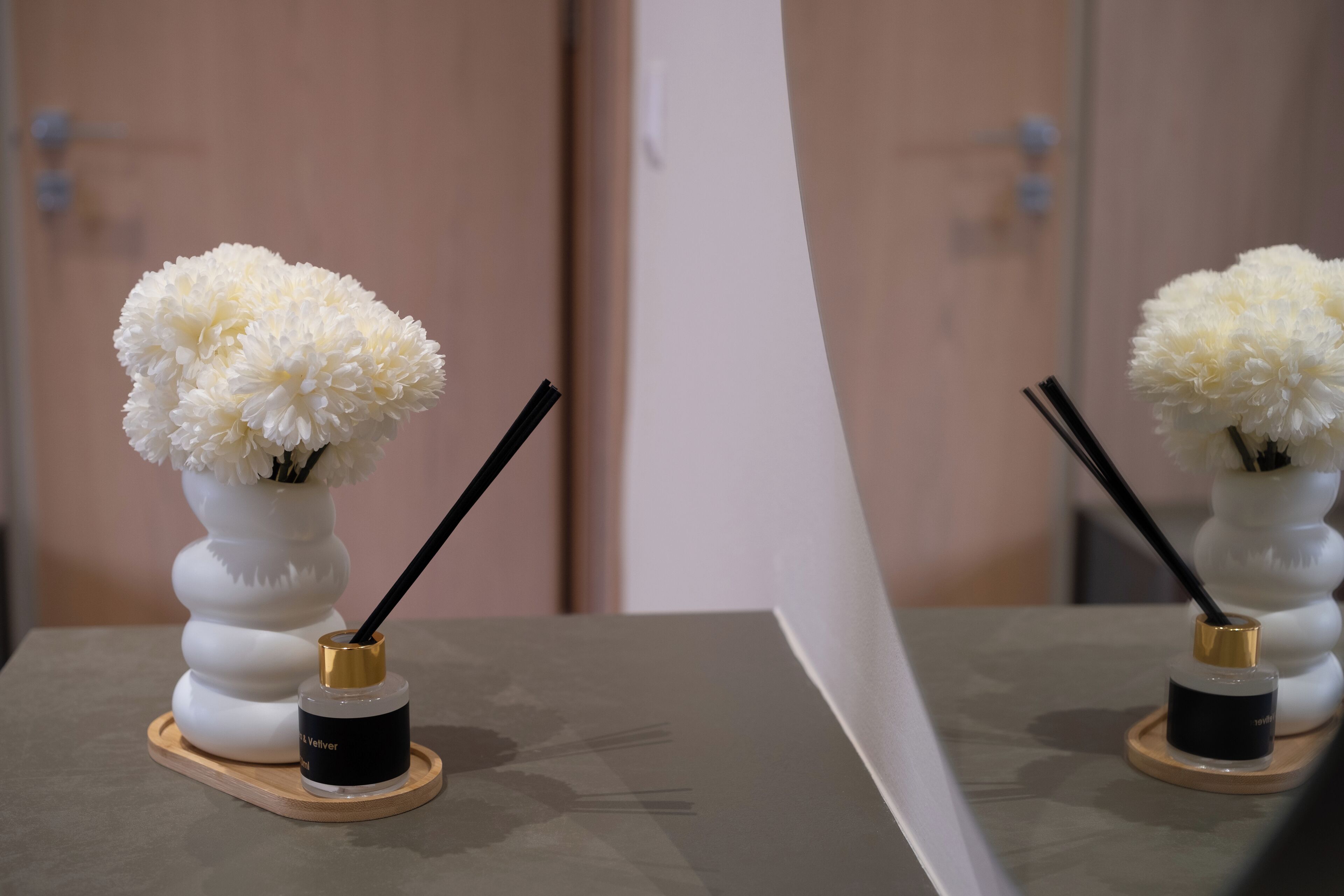 Two white vases with flowers and black incense sticks on a wooden tray.