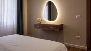 A bedroom with a bed, a bedside table with a mirror, and a nightstand.