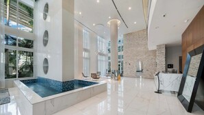 Un moderno vestíbulo de hotel con una amplia piscina interior, suelo de mármol y una recepción.