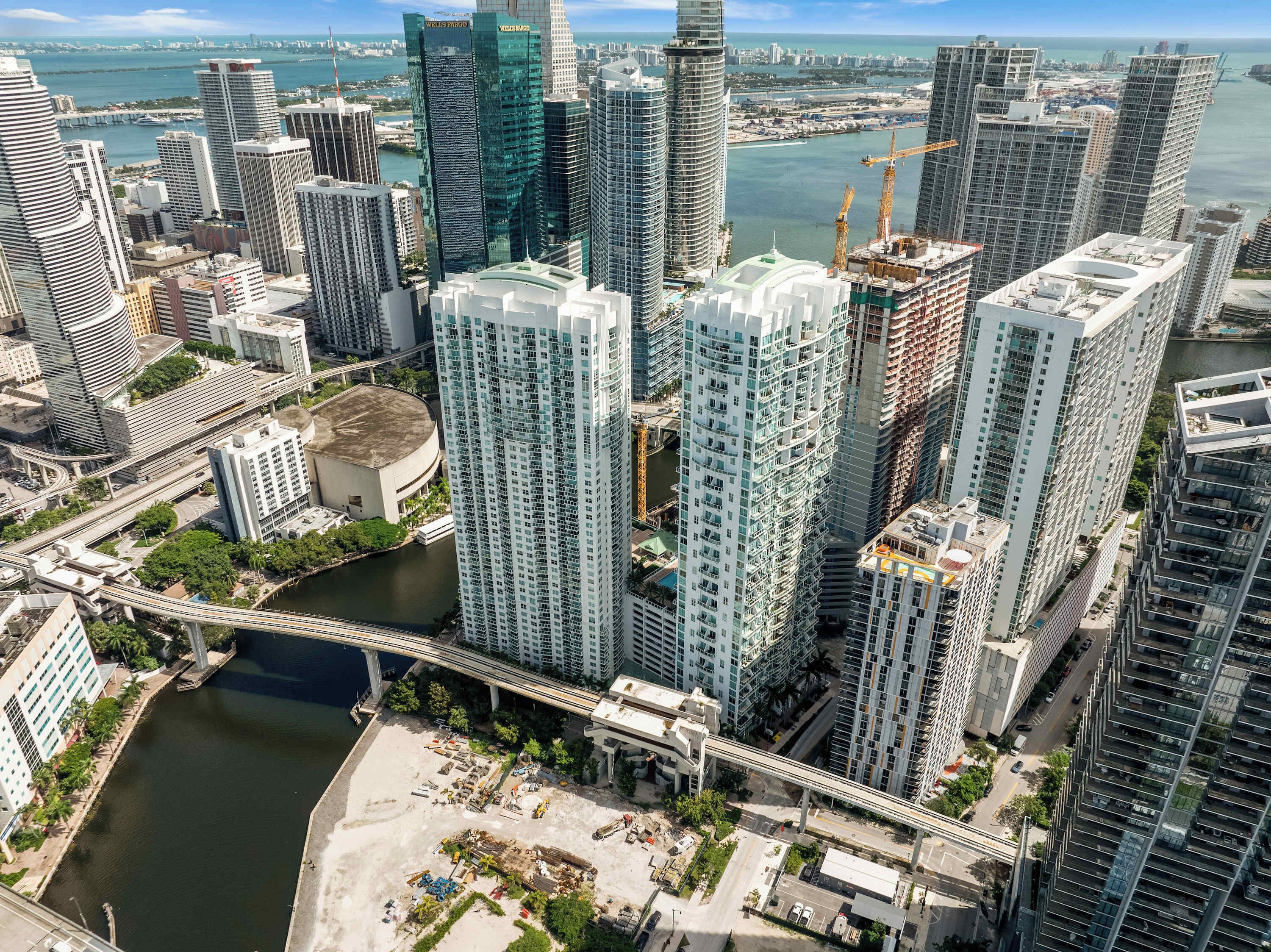 A high-rise building with a modern architectural design, a river running through the city, and a bridge connecting different parts of the area.