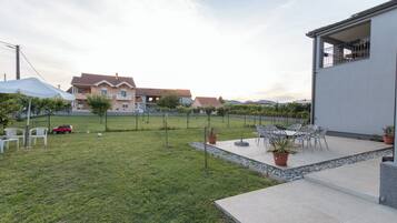 A residential backyard with a patio, outdoor furniture, a red car, and a large house in the background.
