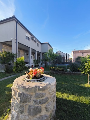 Un bâtiment moderne avec un pilier en pierre au premier plan, une pelouse bien entretenue et un ciel bleu dégagé.