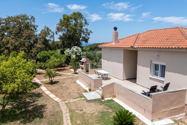 A house with a tiled roof, a patio with chairs, and a garden with trees and shrubs.