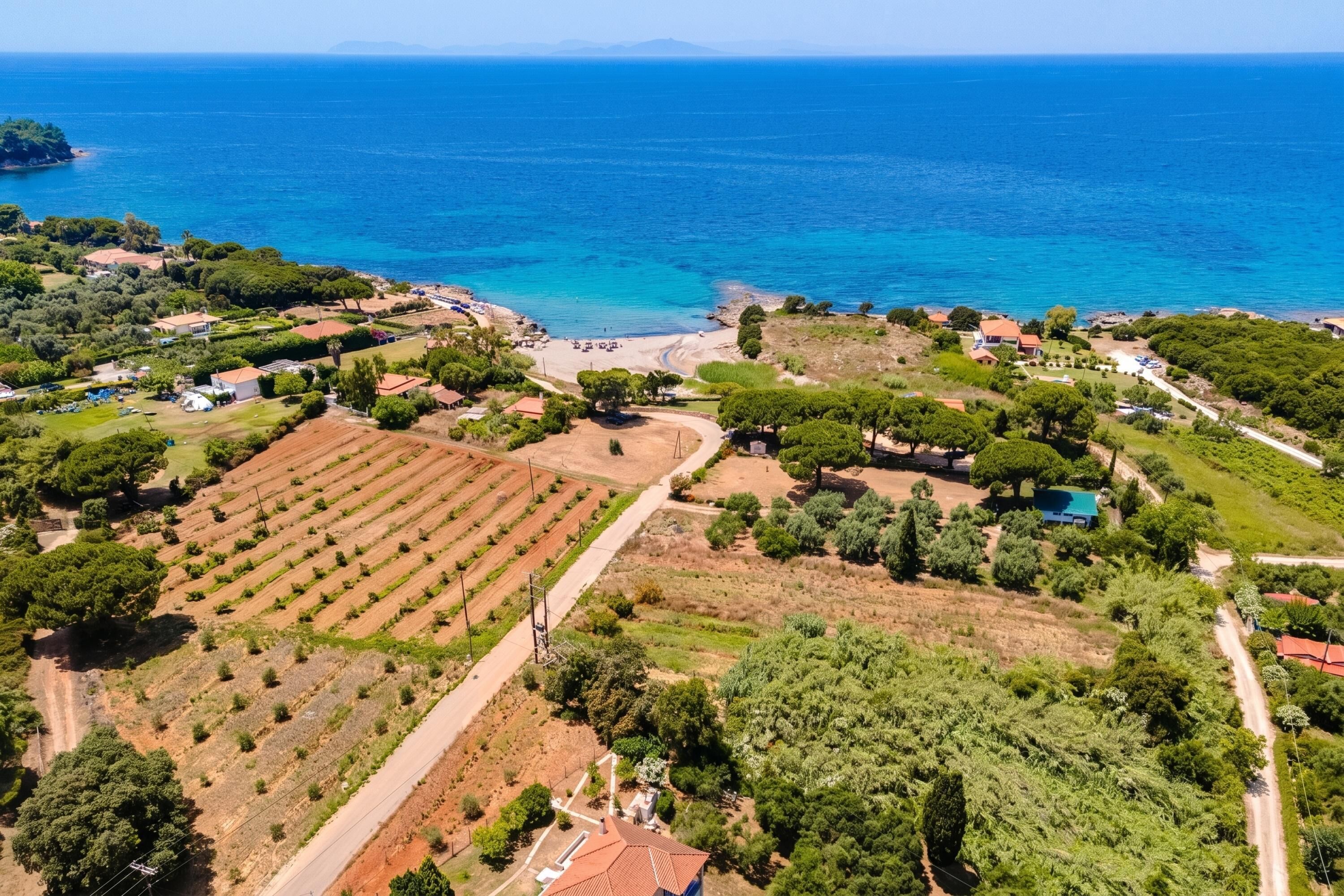 An aerial view of a coastal area with terraced fields, a beach, and residential buildings.