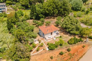 An aerial view of a house surrounded by dense greenery, with a red-tiled roof and a visible patio area. - To Pournari Beachside Garden House (Pyrgos)
