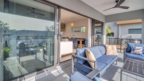 A modern outdoor living area with a glass sliding door, a ceiling fan, and blue furniture. - Heated Saltwater Pool, Walk2 Beach, Pool Table,  Game Room, Play Station 5, 2 75" TVs (Indian Rocks Beach)