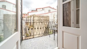 A balcony with a wrought iron gate, a tiled floor, and a view of buildings with red roofs.