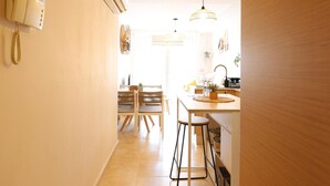 A bright kitchen with a dining area, featuring a wooden table, chairs, and a hanging light fixture.