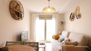 A living room with a sofa, a dining table, chairs, a TV, and a hanging light fixture.
