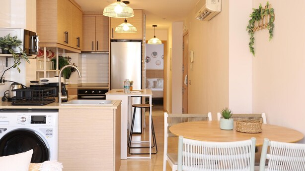 A modern kitchen with a built-in washer, a dining area with a round table and wicker chairs, and pendant lighting.