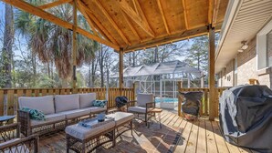 An outdoor deck with a covered seating area, including a sofa and chairs, a grill, and a pool in the background. - The Abuela House w/ pool Near Airport & Ft Moore (Columbus)