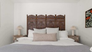 A bed with a wooden headboard, two bedside tables with lamps, and a wall art piece. - The Abuela House w/ pool Near Airport & Ft Moore (Columbus)