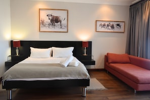 A hotel room with a large bed, two bedside tables with lamps, a red sofa, and two framed pictures on the wall. - Bergwood Inn (Groot Brakrivier)