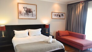 A hotel room with a large bed, a red sofa, and two framed pictures on the wall. - Bergwood Inn (Groot Brakrivier)