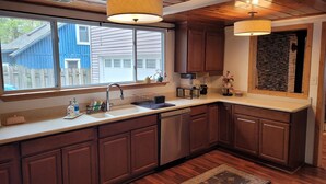 A kitchen with wooden cabinets, a sink, a stove, and a window overlooking a blue house.