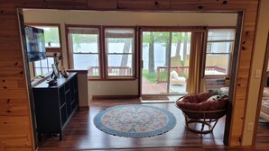 A room with a wooden floor, a round rug, a wicker chair, and a view of a deck and water outside.