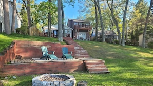 A backyard with a fire pit, two Adirondack chairs, and a wooden deck.