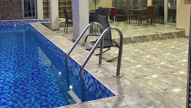 A swimming pool with a tiled edge and metal handrails, surrounded by a tiled floor and glass walls. - Camas Hotels  (Abeokuta)