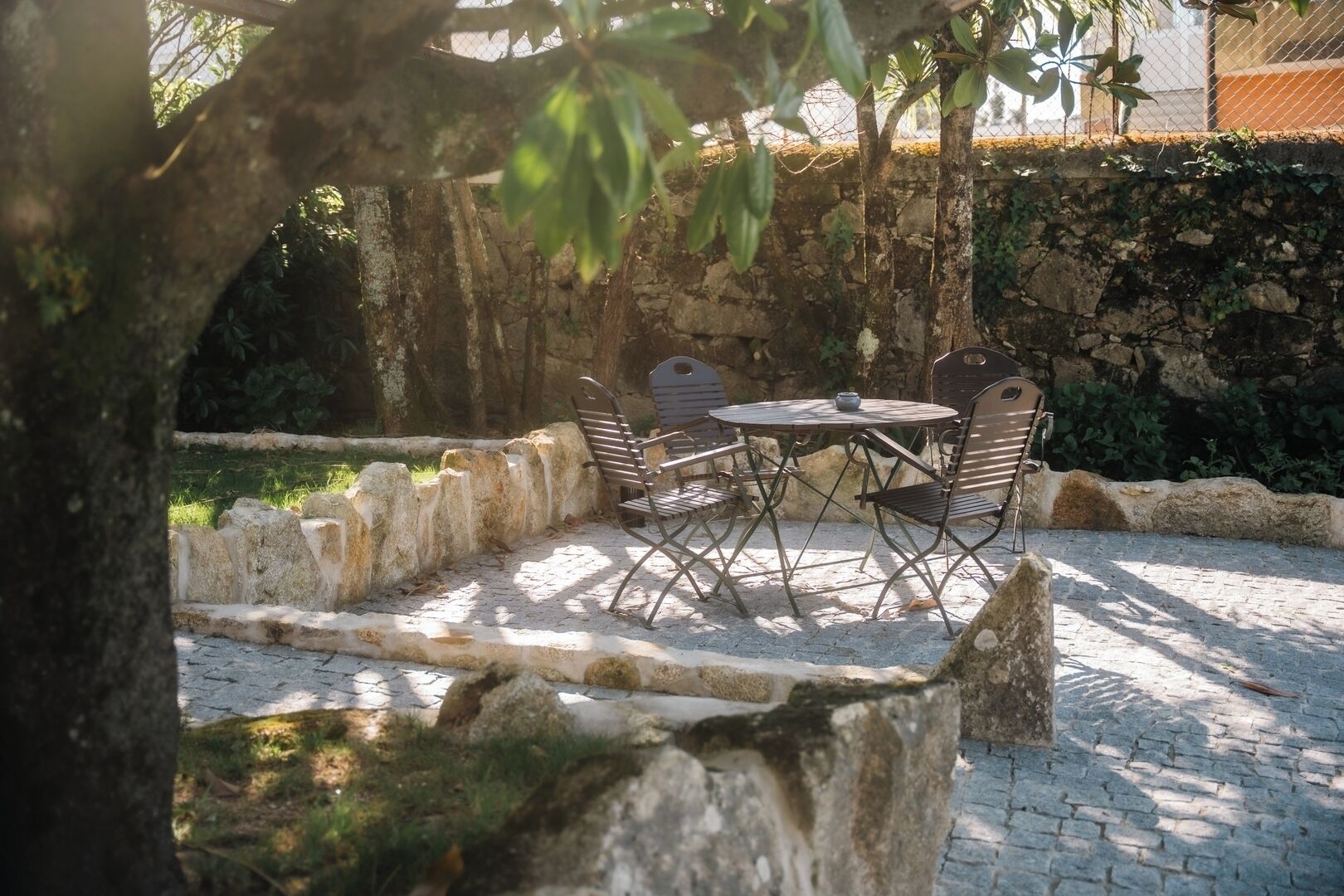 Un espace extérieur aménagé avec des sièges, un mur en pierre, une table en métal et des chaises en métal.