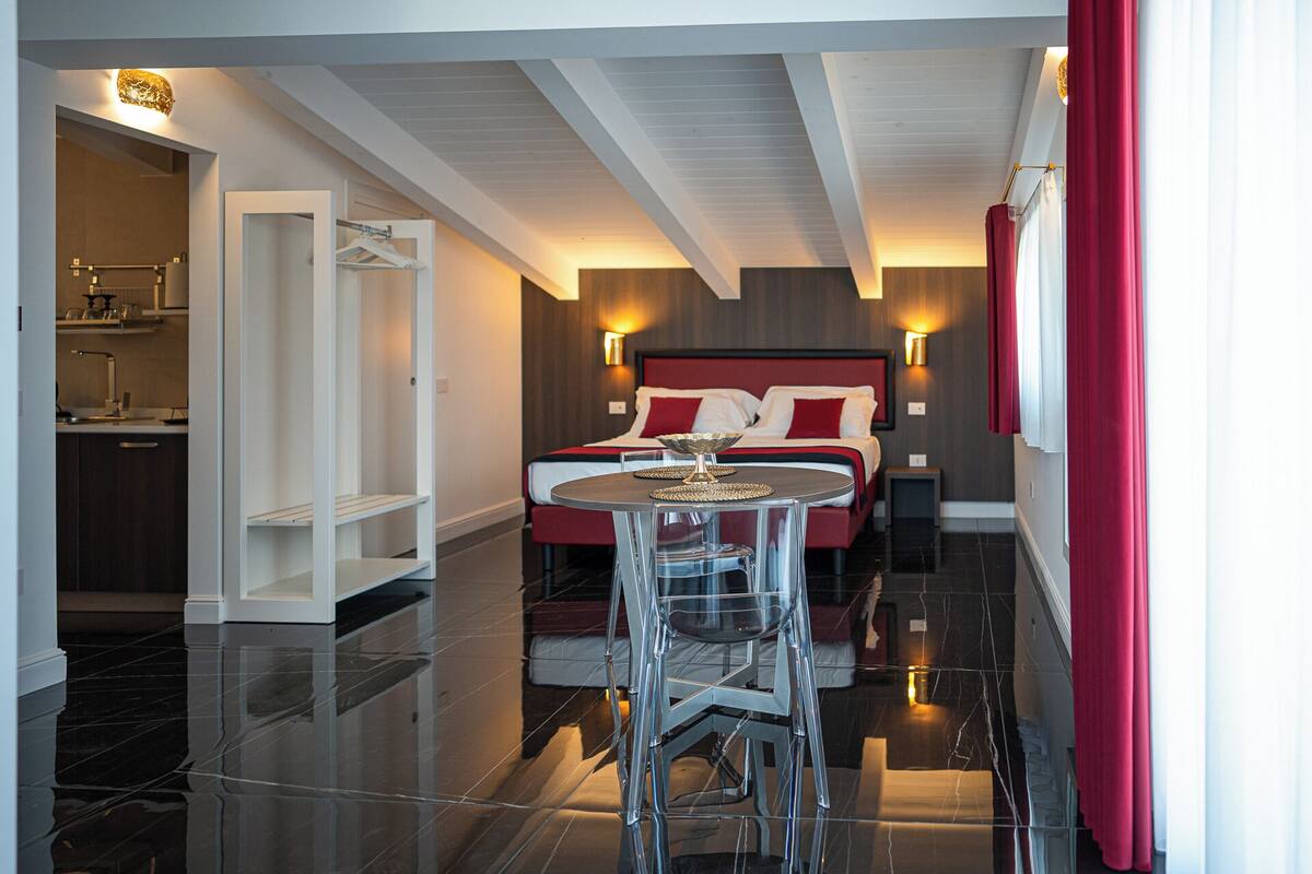 A modern hotel room with a bed, a dining table, and a kitchen area.