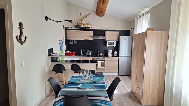 A compact kitchen with modern appliances, a dining area with a striped tablecloth, and a rustic ceiling beam.