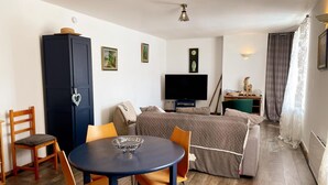 Ein kleines Hotelzimmer mit Bett, Fernseher, kleinem Tisch mit Stühlen, Kleiderschrank und einem Fenster mit Vorhängen.
