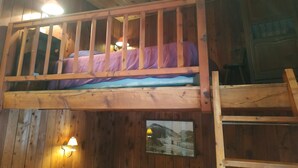A bunk bed with a wooden frame and a mattress, a wooden wall with a picture, and a small table with a lamp. - Studio 3 ppl - Ski-in/ski-out - Val d'Isère Center - Wifi (Val-d'Isère)