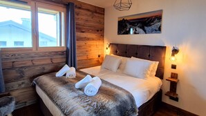A bedroom with a wooden wall, a bed with white linens, a mounted painting, and a hanging light fixture. - Cozy apartment in Les Gets, 3 bedrooms, Wi-Fi (Les Gets)