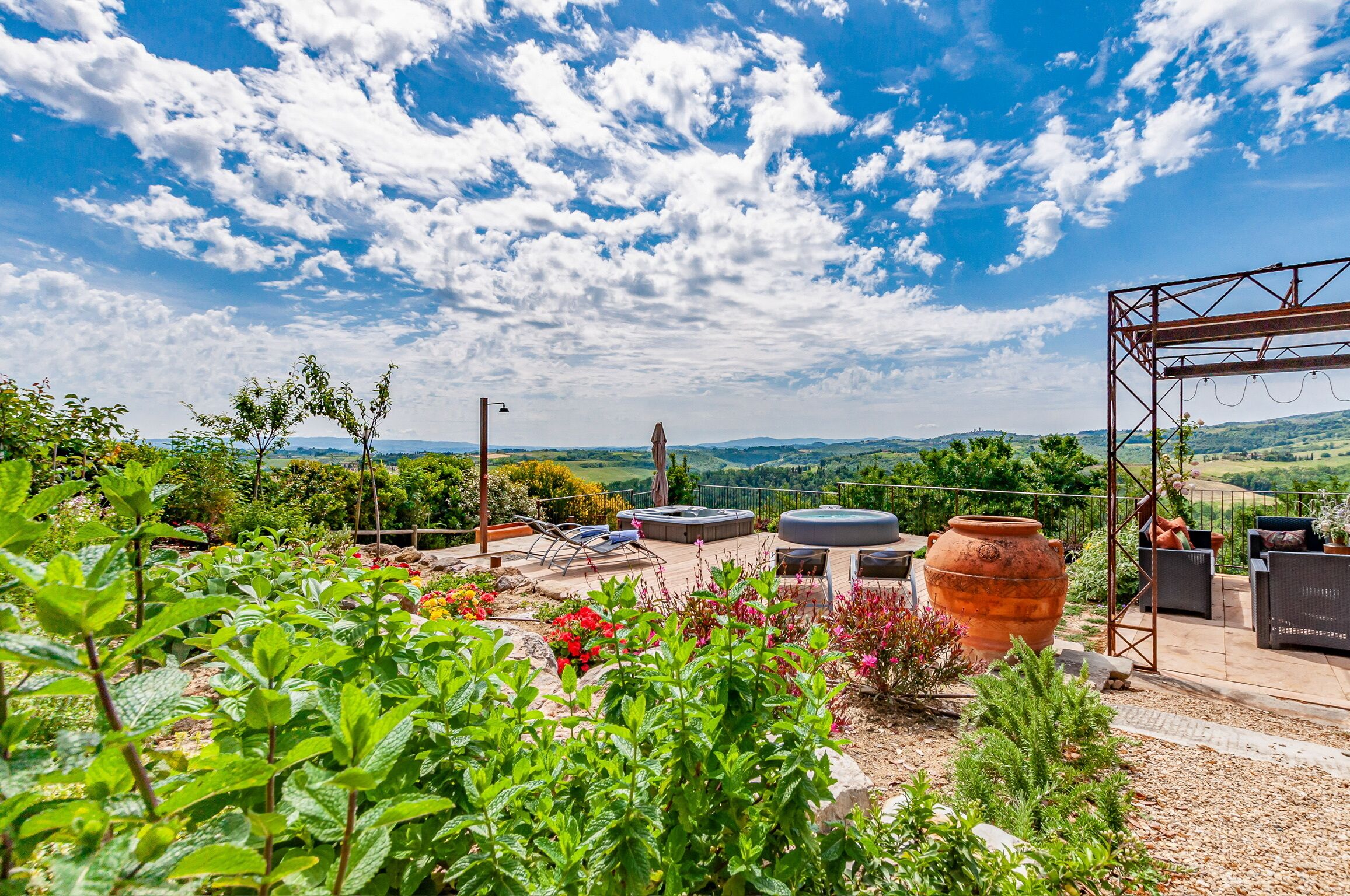 Un patio jardín con mobiliario exterior, una gran maceta de terracota y vistas a colinas ondulantes.