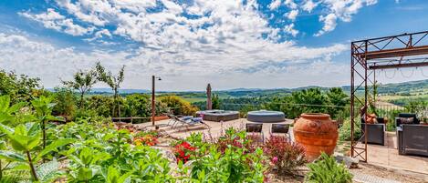 Un patio jardín con mobiliario exterior, una gran maceta de terracota y vistas a colinas ondulantes.