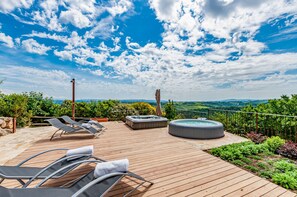 A wooden deck with lounge chairs, a hot tub, and a scenic view of the landscape.
