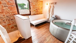 Une pièce avec un mur en pierre, un banc blanc, une baignoire et un plancher en bois.