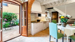 Une cuisine avec des meubles blancs, une arche en briques et un coin repas avec des chaises vertes.