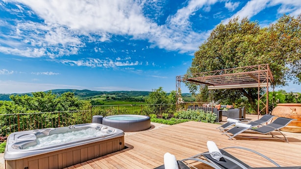 Une terrasse en bois avec un jacuzzi, des chaises longues et une pergola agrémentée de mobilier d’extérieur.
