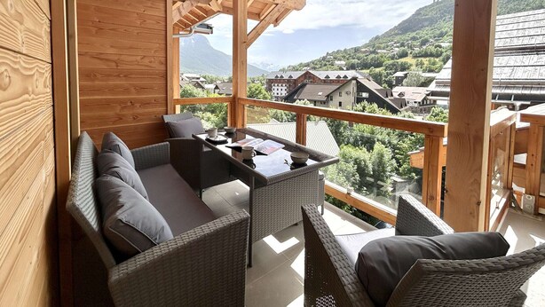 Un balcon agrémenté de meubles en osier, un plafond en bois et une vue sur un village de montagne.
