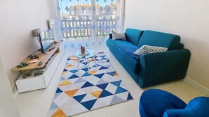 A compact living space with a sofa, a small table, and a decorative rug. - Cozy apartment 4 pax near sea with parking (Courseulles-sur-Mer)