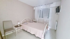A bedroom with a bed, a chair, a bedside table, and a window with curtains. - Cozy apartment 4 pax near sea with parking (Courseulles-sur-Mer)