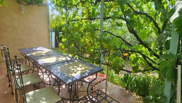 Un patio al aire libre con una mesa y sillas, rodeado de abundante vegetación y un cielo despejado.