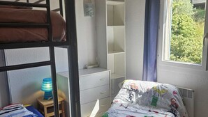 Habitación tipo dormitorio con literas, un escritorio, una silla y ventana con vista a zonas verdes.