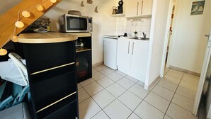 A compact kitchen with white cabinets, a microwave, and a small refrigerator. There are string lights above the counter and a clock on the wall. - 3-room Pavilion with Terrace, Near the Beach (Narbonne)