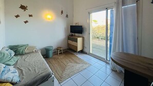 A bedroom with a bed, a TV, a small stool, and a sliding glass door leading to a garden. - 3-room Pavilion with Terrace, Near the Beach (Narbonne)