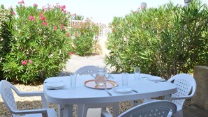 An outdoor dining area with a round table and white chairs, surrounded by greenery and a clear view of the sky. - 3-room Pavilion with Terrace, Near the Beach (Narbonne)