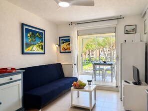 A living room with a sofa, a small table with fruit, a TV, and a sliding glass door to a balcony.