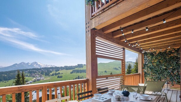 Une terrasse en bois avec une table dressée pour le repas, offrant une vue sur un paysage montagneux.