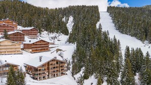 Une station de ski dotée de plusieurs chalets en bois, d’une pente enneigée et d’une forêt de conifères dense.