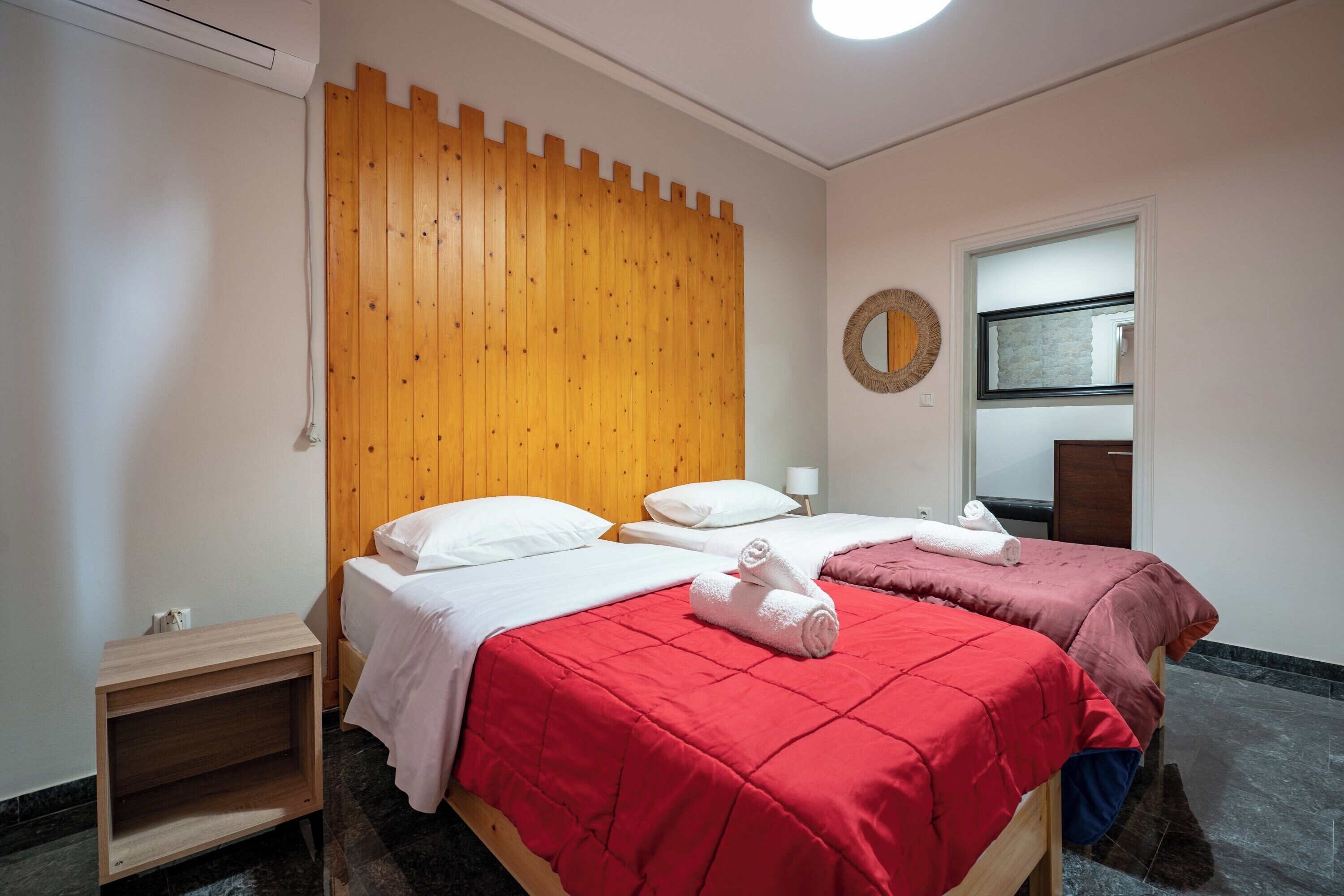 A hotel room with two beds, a wooden headboard, a mirror, and a small wooden nightstand.