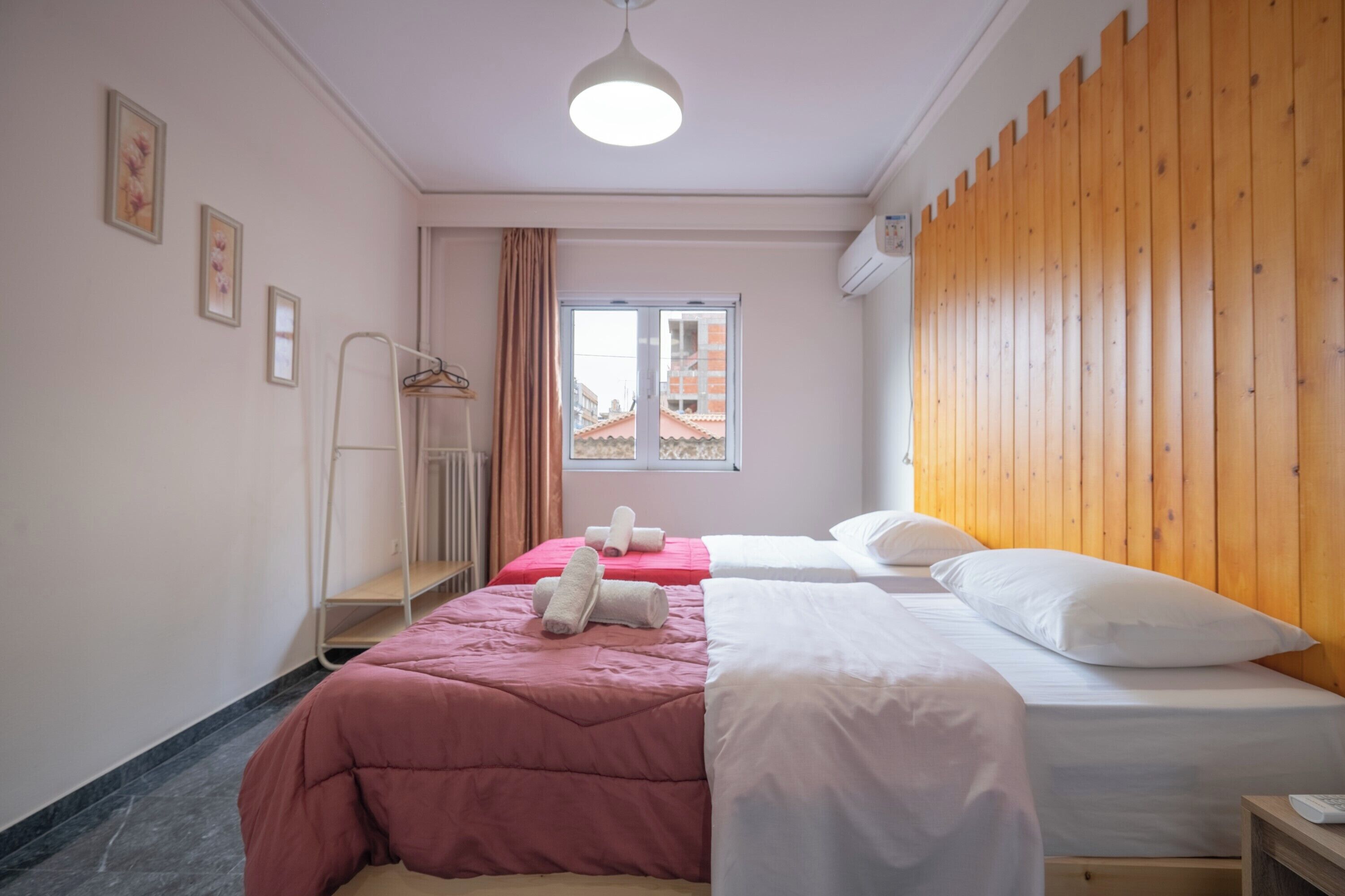 A hotel room with two beds, a wooden headboard, a window with a view, and a radiator.