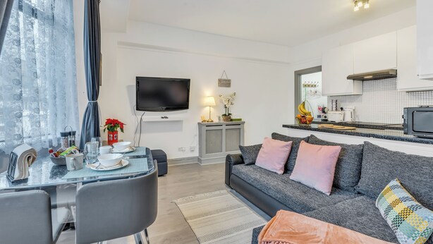 Un salon moderne avec un canapé gris, une table à manger et un téléviseur fixé au mur.